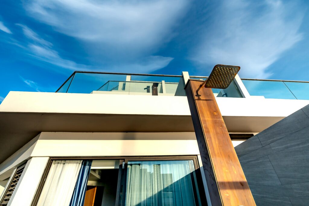 Contemporary terrace design with glass railings and outdoor shower against a vivid sky.